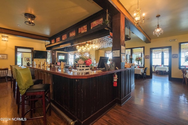 bar with pendant lighting, a notable chandelier, beam ceiling, and dark hardwood / wood-style flooring