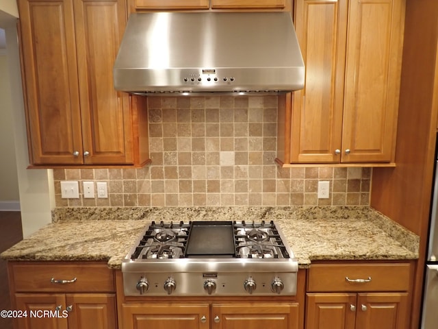 kitchen with stainless steel gas stovetop, light stone counters, decorative backsplash, and range hood