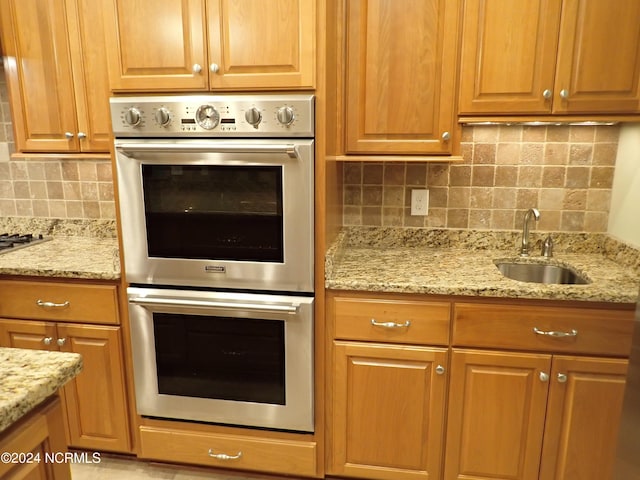 kitchen with tasteful backsplash, light stone counters, sink, and stainless steel double oven