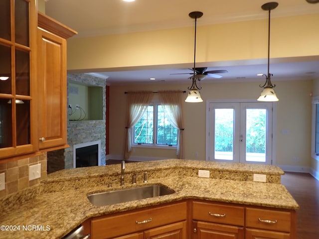 kitchen featuring a stone fireplace, sink, hanging light fixtures, decorative backsplash, and ceiling fan