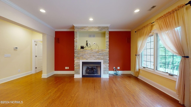 unfurnished living room with a stone fireplace, crown molding, and wood-type flooring