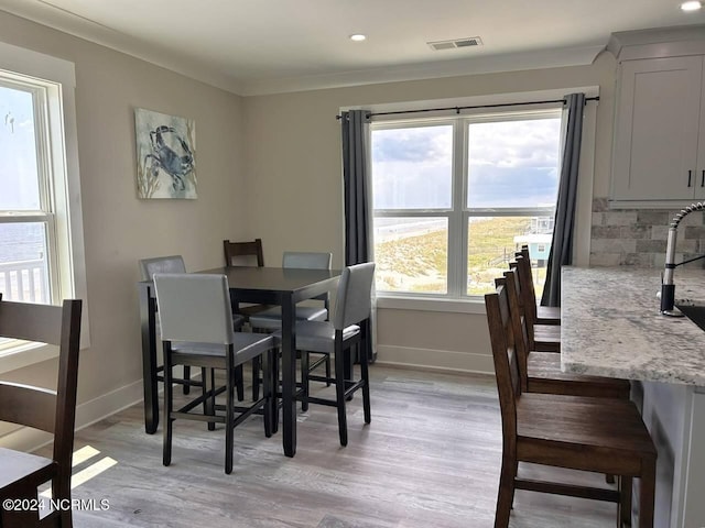 dining area with light wood-type flooring, baseboards, visible vents, and ornamental molding