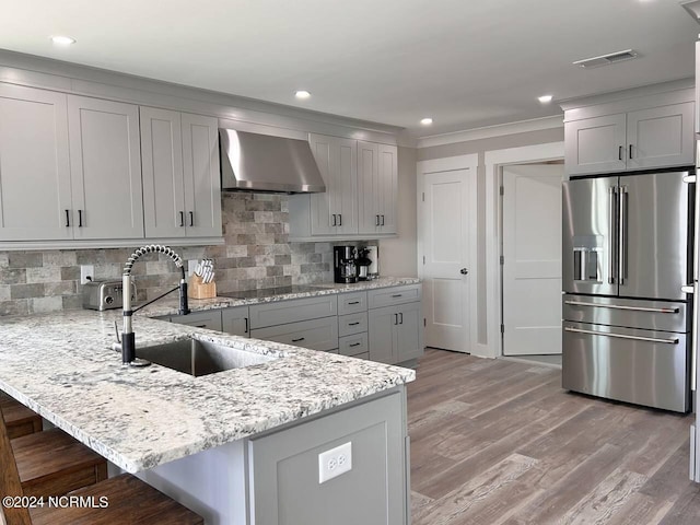 kitchen with wall chimney exhaust hood, high end refrigerator, a sink, and a kitchen breakfast bar