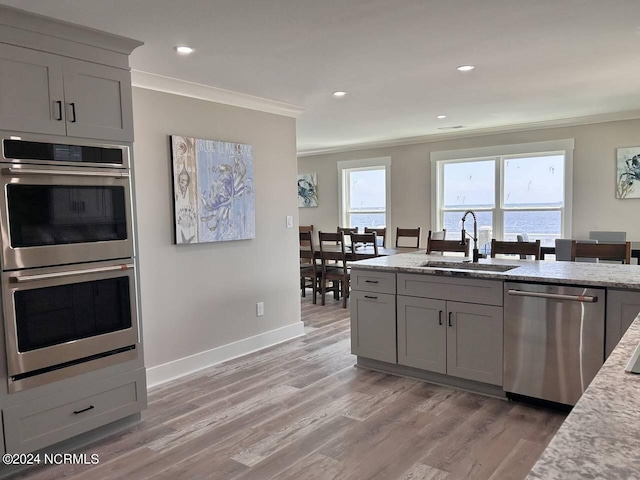 kitchen featuring appliances with stainless steel finishes, a sink, light stone counters, and crown molding