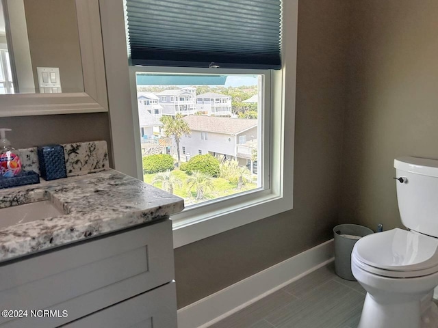 half bathroom with tile patterned flooring, baseboards, vanity, and toilet