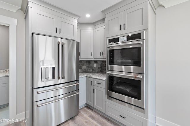 kitchen featuring stainless steel appliances, gray cabinets, decorative backsplash, and light stone counters