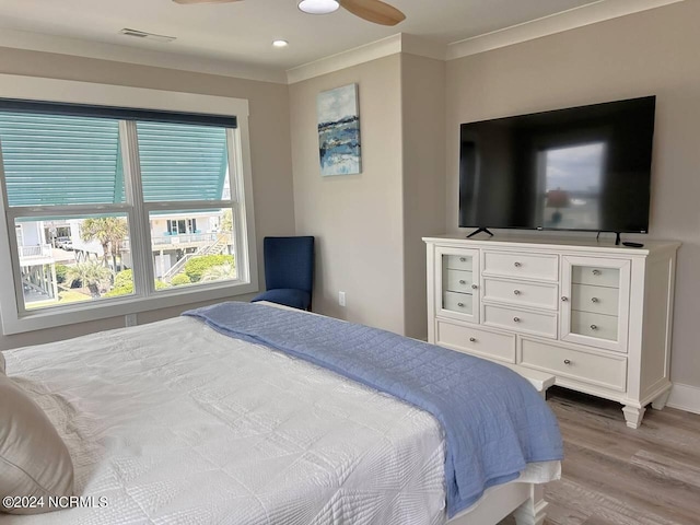 bedroom featuring wood finished floors, a ceiling fan, baseboards, visible vents, and crown molding