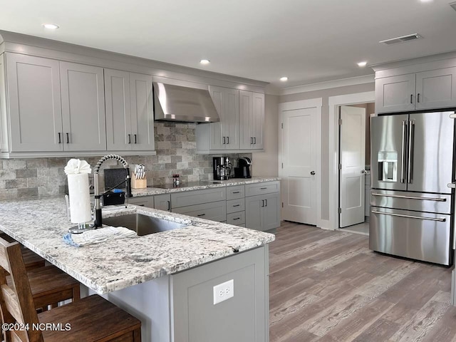 kitchen featuring a breakfast bar area, high end fridge, gray cabinets, visible vents, and wall chimney range hood