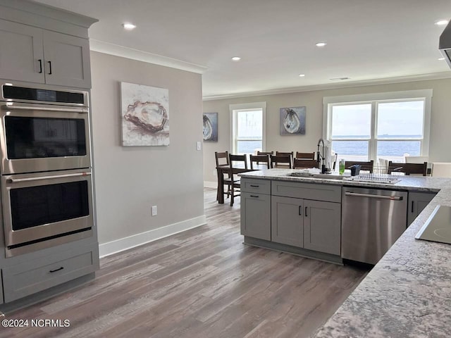 kitchen featuring light stone counters, stainless steel appliances, a water view, gray cabinets, and crown molding