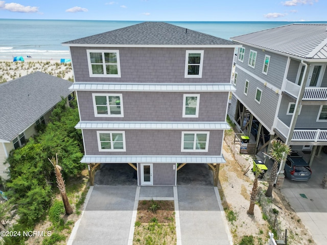 view of front of property featuring a beach view, concrete driveway, metal roof, roof with shingles, and a water view