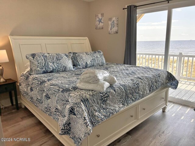 bedroom featuring dark wood-style floors, a water view, and access to exterior