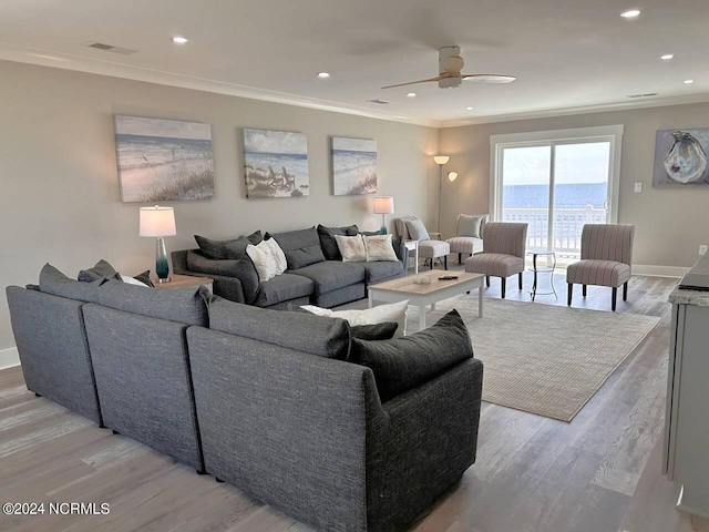 living room featuring a water view, light wood finished floors, baseboards, and crown molding