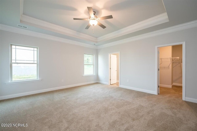 unfurnished bedroom with a raised ceiling, crown molding, a spacious closet, and ceiling fan