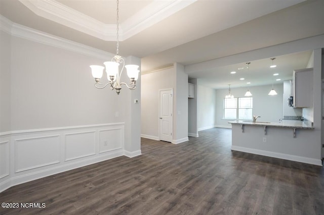 interior space featuring a raised ceiling, ornamental molding, dark wood-type flooring, and an inviting chandelier