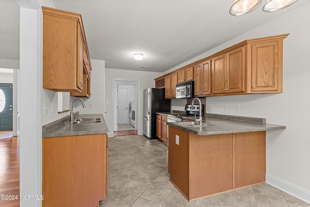 kitchen with washer / clothes dryer, sink, light tile patterned floors, kitchen peninsula, and stainless steel appliances