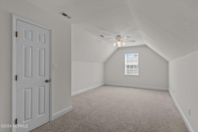 additional living space with vaulted ceiling, ceiling fan, light carpet, and a textured ceiling