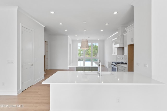 kitchen featuring white cabinets, a sink, light countertops, light wood-style floors, and high end range