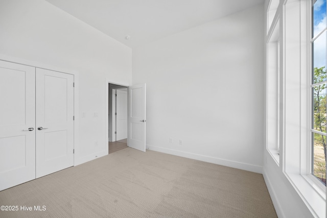unfurnished bedroom featuring a closet, a towering ceiling, light colored carpet, and baseboards