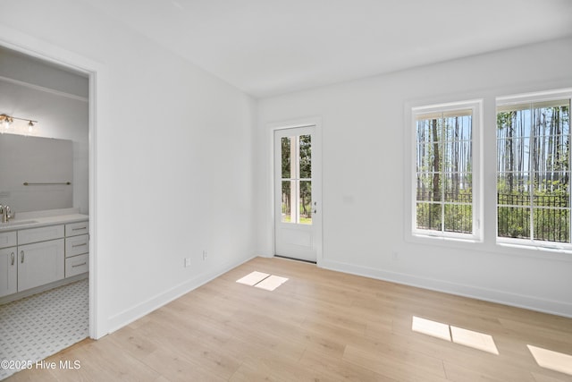unfurnished bedroom featuring a sink, ensuite bathroom, baseboards, and light wood finished floors