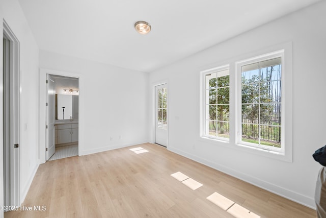 unfurnished bedroom featuring light wood-type flooring, baseboards, and ensuite bath