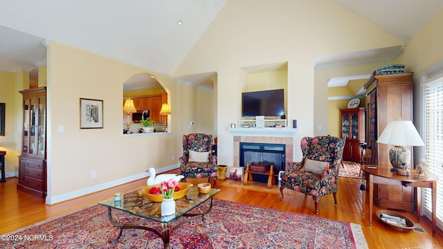 living room featuring high vaulted ceiling, wood-type flooring, a tiled fireplace, and crown molding