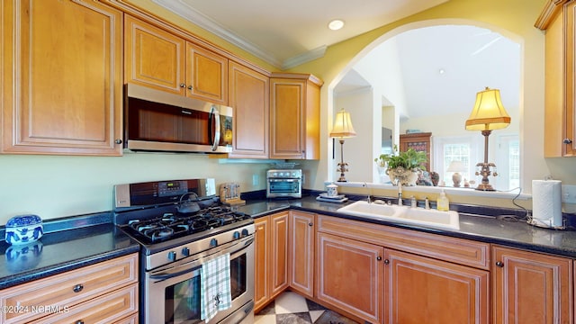 kitchen featuring dark countertops, ornamental molding, stainless steel appliances, and a sink