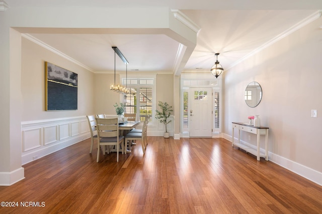 dining room with a decorative wall, an inviting chandelier, ornamental molding, wood finished floors, and baseboards