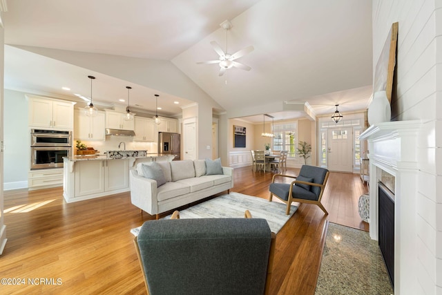 living area featuring a fireplace, a ceiling fan, ornamental molding, high vaulted ceiling, and light wood-type flooring