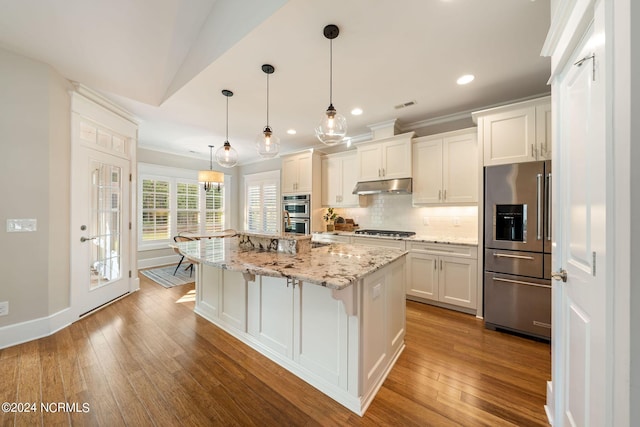 kitchen with tasteful backsplash, appliances with stainless steel finishes, white cabinetry, under cabinet range hood, and hardwood / wood-style floors