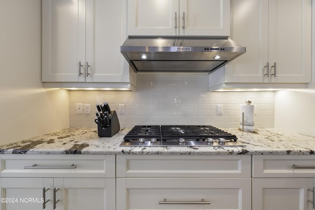 kitchen featuring white cabinets, decorative backsplash, light stone counters, stainless steel gas stovetop, and exhaust hood