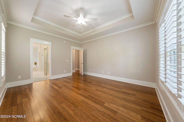 unfurnished bedroom featuring a tray ceiling, multiple windows, and wood-type flooring