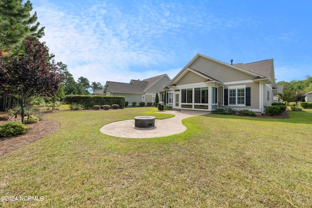 back of property featuring a fire pit, a patio, a yard, and a sunroom