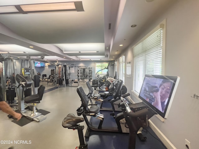 gym with a tray ceiling and baseboards