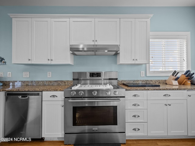 kitchen featuring white cabinets, stainless steel appliances, dark stone counters, and wall chimney range hood