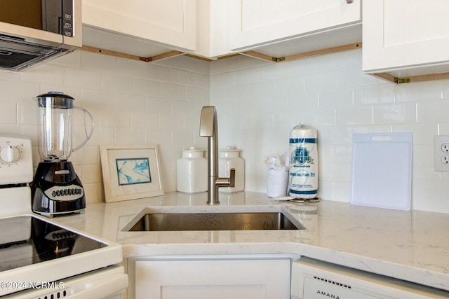 kitchen with tasteful backsplash, light stone countertops, range, and white cabinets