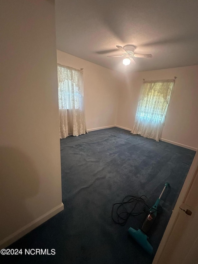 unfurnished room with ceiling fan and dark colored carpet