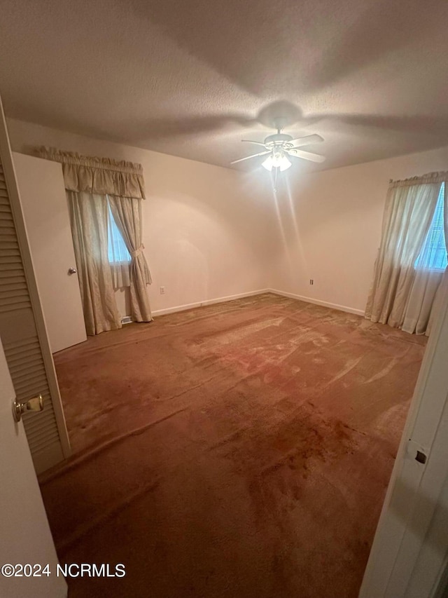 carpeted spare room with ceiling fan, a wealth of natural light, and a textured ceiling