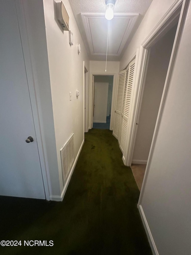 hall featuring dark carpet and a textured ceiling