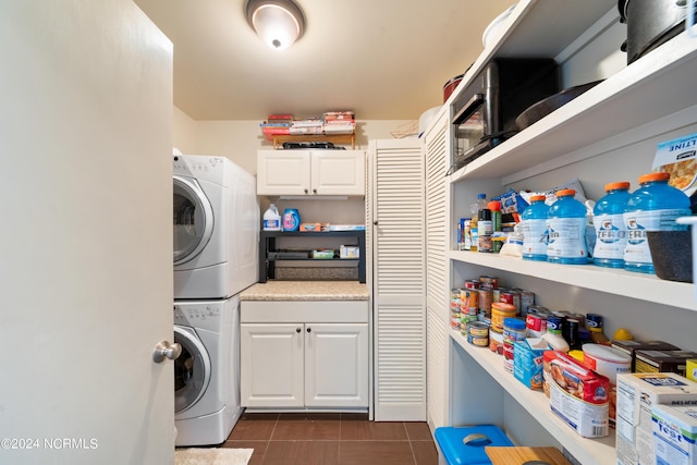 laundry area featuring dark tile patterned floors, cabinet space, and stacked washer / drying machine