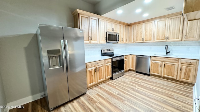 kitchen featuring stainless steel appliances, a sink, visible vents, light wood-style floors, and light brown cabinetry