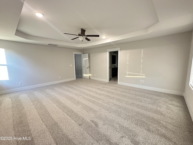 carpeted empty room with ceiling fan and a tray ceiling