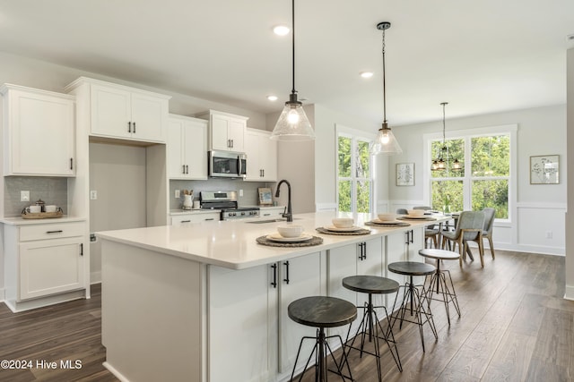 kitchen with a kitchen island with sink, stainless steel appliances, hanging light fixtures, sink, and white cabinetry