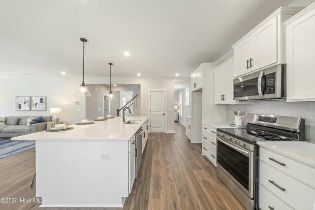 kitchen featuring hanging light fixtures, a center island with sink, decorative backsplash, white cabinetry, and appliances with stainless steel finishes