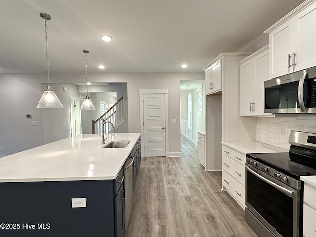 kitchen featuring decorative light fixtures, stainless steel appliances, a center island with sink, white cabinets, and sink