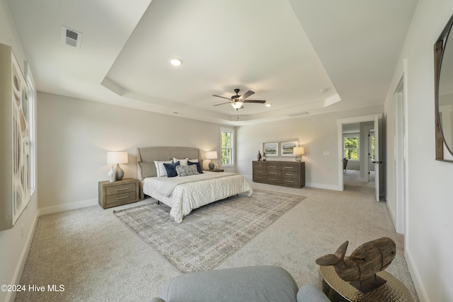 bedroom featuring a raised ceiling, ceiling fan, and light colored carpet