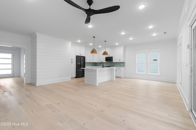 kitchen featuring black appliances, a center island with sink, light countertops, light wood-style floors, and white cabinetry