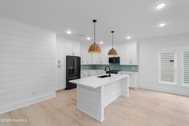 kitchen featuring light wood-type flooring, black appliances, a sink, white cabinets, and light countertops