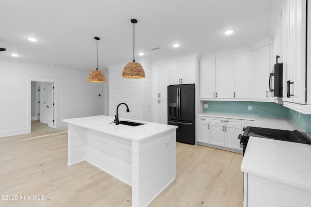 kitchen with black appliances, white cabinets, light wood finished floors, and a sink