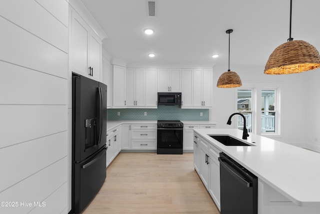 kitchen with a sink, decorative backsplash, black appliances, light countertops, and white cabinetry