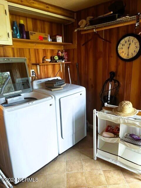 washroom featuring light tile patterned flooring, washing machine and clothes dryer, and wood walls